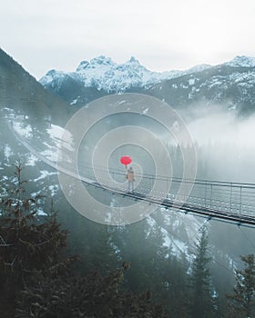 A man with a red umbrella crosses a suspension bridge in the mountains