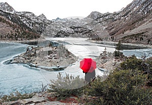 A man with a red umbrella stands on the lake in the Sierras of California