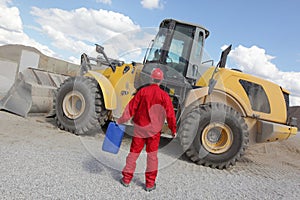 Man in red uniform with petrol can, bulldozer in background,back view