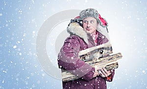 Man in red winter clothes carries firewood for the stove in his hands, snow is falling on a blue background