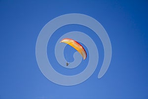 A man on a red yellow white paraglide in a clear blue sky