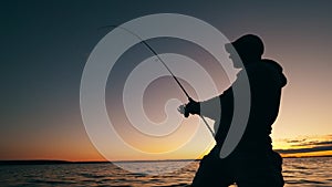 A man is reeling up a fishing pole in a sunset lake