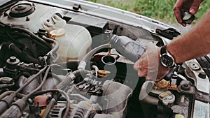 A man refills engine oil in a car. Close-up of hands