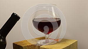 The man refills the wine glass. Red wine in a glass goblet. Stands on wooden chocks. Rotates on a light background. Close-up shot