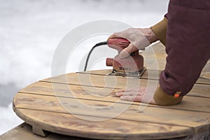 Man Refinishing an outdoor cedar table with palm sander. photo