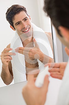 Man with reflection putting moisturizer on face