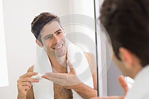 Man with reflection putting moisturizer on his face