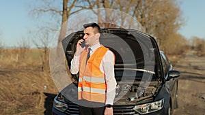 Man with reflective vest calling by phone about breakdown in her modern car. Emergency stop sign. Car accident on the