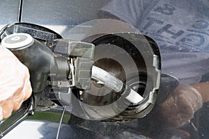 A man refueling a black car with diesel fuel at a gas station. Refueling nozzle close up and jet of fuel.