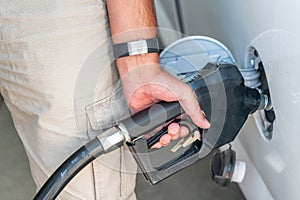 Man refuelling a car at a petrol station, detail on hand and pump