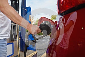 Man refuses his red car with gasoline at a gas station. Hand and black refueling gun close up