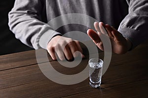 Man refusing to drink vodka at wooden table, closeup. Alcohol addiction