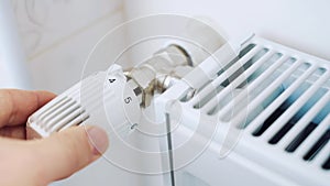 A man regulates the temperature in the house with a thermostat on the radiator