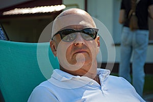 Man relax on summer sunbed outdoor. Summer vacation. Summertime at poolside. Bold man relax in sunbed in the chill area. Vacation