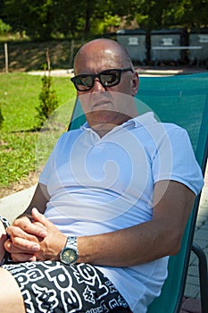 Man relax on summer sunbed outdoor. Summer vacation. Summertime at poolside. Bold man relax in sunbed deckchair in the park.