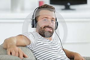 man relaxes with headphones and laptop on sofa