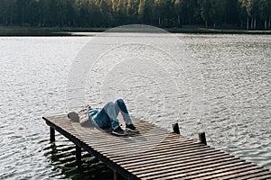 A man relaxes lying on a wooden boat dock on a lake in autumn