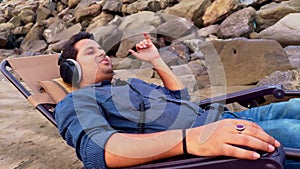 Man relaxing on a beach chair listening music with headphones eyes closed enjoying a peaceful moment on a sandy beach