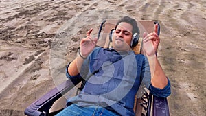 Man relaxing on a beach chair listening music with headphones eyes closed enjoying a peaceful moment on a sandy beach