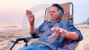 Man relaxing on a beach chair listening music with headphones eyes closed enjoying a peaceful moment on a sandy beach