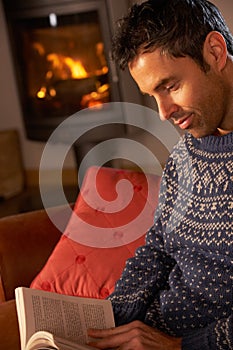 Man Relaxing With Book By Cosy Log Fire