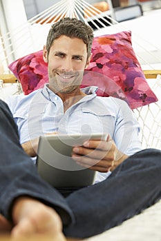 Man Relaxing In Garden Hammock Using Digital Tablet