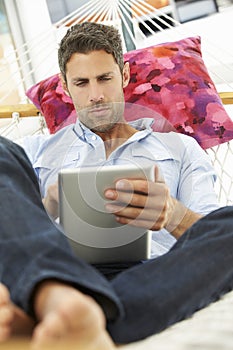 Man Relaxing In Garden Hammock Using Digital Tablet