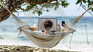 A man is relaxing on a hammock by the ocean, using his laptop and cell phone