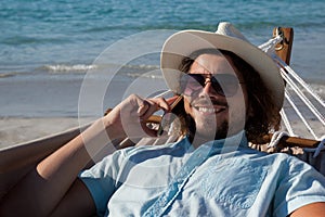 Man relaxing on hammock and talking on mobile phone on the beach