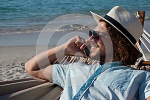 Man relaxing on hammock and talking on mobile phone on the beach