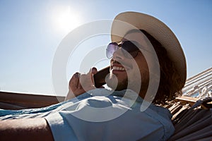 Man relaxing on hammock and talking on mobile phone on the beach