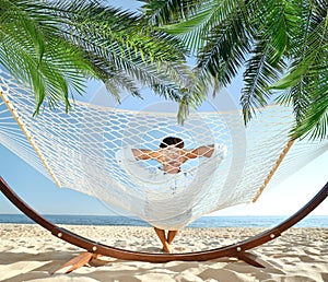 Man relaxing in hammock under palm leaves on sunlit beach