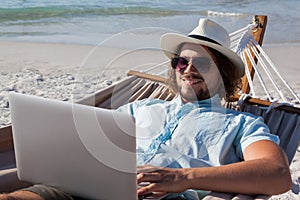 Man relaxing on hammock and using laptop on the beach