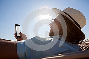 Man relaxing on hammock and using mobile phone on the beach