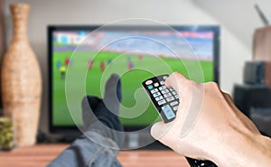 Man is relaxing with legs on table and is watching football match on TV