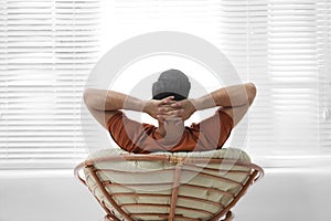 Man relaxing in papasan chair near window at home