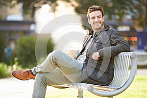 Man Relaxing On Park Bench With Takeaway Coffee