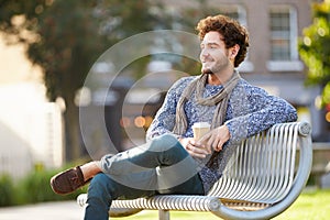 Man Relaxing On Park Bench With Takeaway Coffee