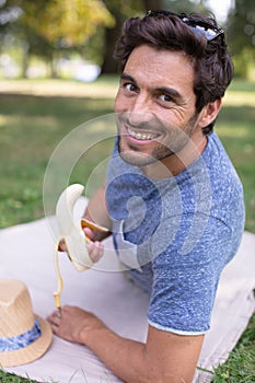 man relaxing in park laying on blanket eating banana
