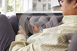 Man Relaxing On Sofa At Home Using Digital Tablet