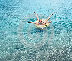 Man relaxing when swims on inflatable pineapple pool ring in crystal clear sea water. Careless vacation concept image