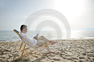 Man relaxing with tablet on the beach sitting on a deckchair