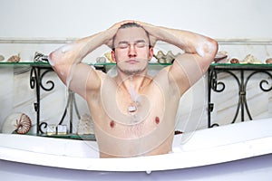 Man relaxing taking a foamy bath. Washes foam from the head. Sexuality and relaxation concept. Guy in bathroom with toiletries on