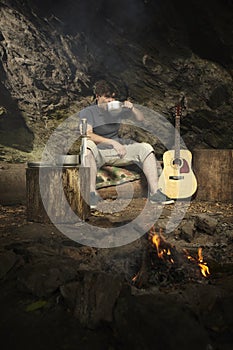 Man relaxing in wilderness with guitar and drinking