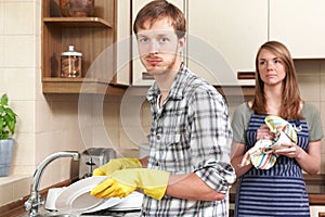 Man Reluctantly Washing Up In Kitchen With Partner