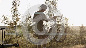 Man removes a road bike from a car bicycle mount at the sunset on a highway