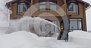 Man removes snow with snowblower in yard at snowfall in slow motion. Back view