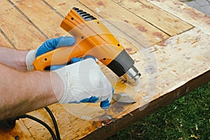 Man removing old varnish from wood using scraper and heat gun.