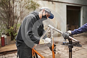 Man removing the paint of an orange bicycle frame during a bike renovation work