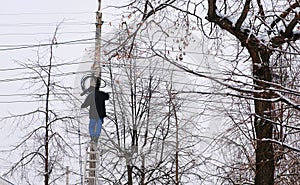 Man repair of power lines in the city in winter. Stands on a ladder with a wire in his hands, back view.